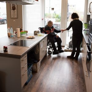 Ein Rollstuhlfahrer in der offenen Küche mit seiner Assistenz am Kochen